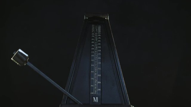 Close-up shot of vintage metronome with golden pendulum beats slow rhythm on the dark background