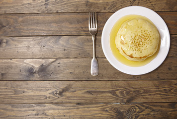 Overhead view of a stack of golden syrup covered hotcakes on a wooden breakfast table background forming a page border