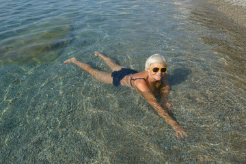 Aged lady is lying in clear transparent water sea beach.