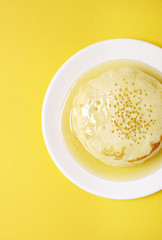 Aerial view of a stack of hotcakes with golden syrup on a bright yellow background