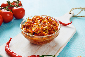 Bolognese sauce in glass bowl on cutting board surrounded by ingredients on blue table