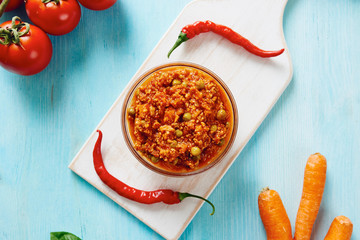 Bolognese sauce in glass bowl on cutting board surrounded by ingredients on blue table