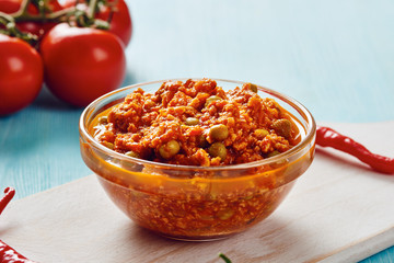 Bolognese sauce in glass bowl on cutting board surrounded by ingredients on blue table