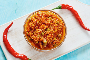 Bolognese sauce in glass bowl on cutting board surrounded by peppers on blue table