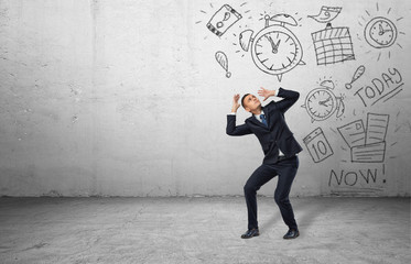 Frightened businessman shielding himself with his hands from the drawings of calendars and clocks