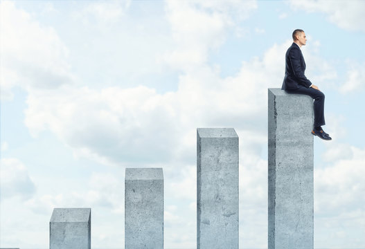 Businessman sitting on highest concrete columns of the chart