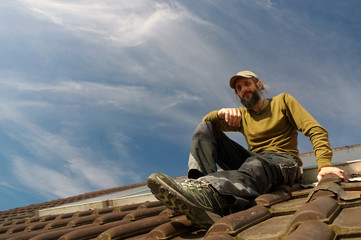 bearded roofer resting on top of a roof sunny day