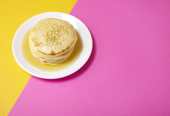 A stack of golden syrup covered pancakes on a bright pink and yellow background forming a page border