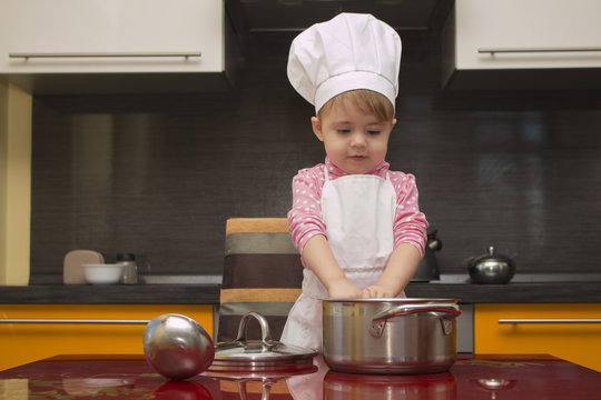 The small child in chef suit helps her mother cook in the kitchen