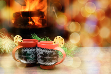 Cup with Christmas ornament near fireplace. Mug in red knitted cloth