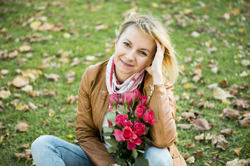 smiling woman with roses sits on the yellow leaves