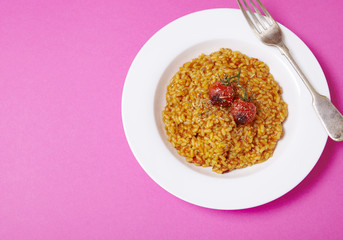 A dinner bowl of tomato risotto on a bright pink background