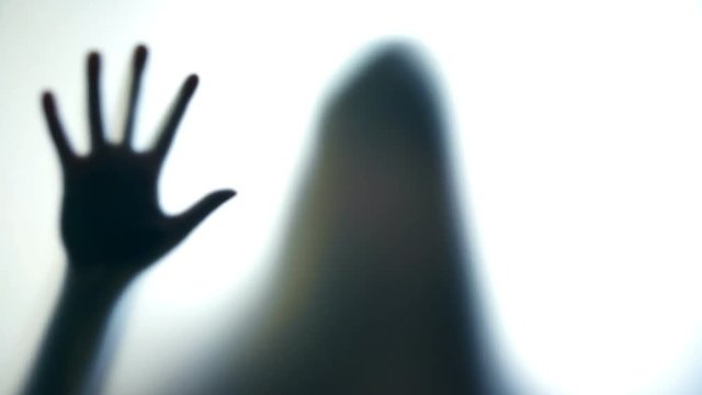 Female silhouette pounding on glass, kidnapped woman lost hope to break free. Scary ghostly creature behind the glass
