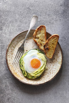 Breakfast with baked egg in zucchini noodles nest with bread toa
