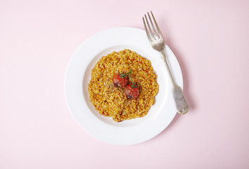 Aerial view of a dinner dish of tomato risotto on a pastel pink background