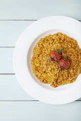 A white dinner dish of tomato risotto on a blue painted table background