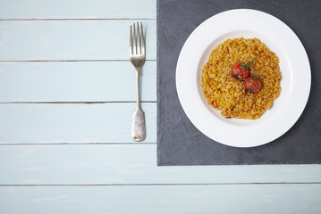 Aerial view of a dinner dish of tomato risotto on a blue wooden table background forming a page border