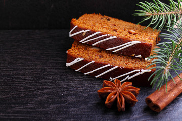 Gingerbread (honey-cake) with raisins decorated with icing, spruce branches, cinnamon sticks, star anise on a black background