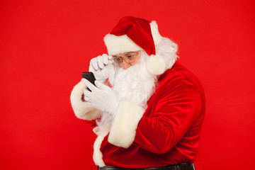 Photo of Santa Claus using mobile phone, on a red background. Christmas