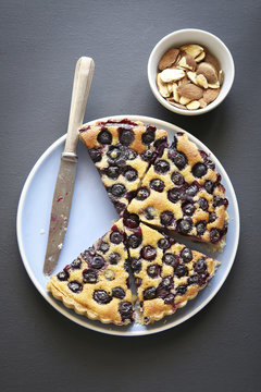 Slices of blueberry tart on a blue plate and roasted almonds.Top