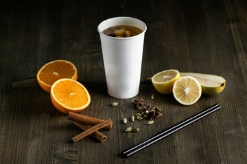 Tea drink in white cup, standing next to an orange, lemon and cinnamon on wooden table