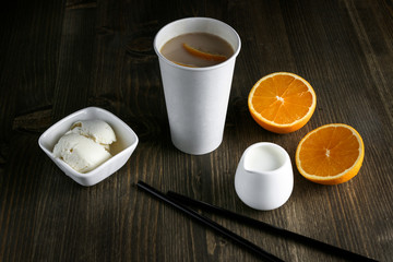 Tea drink in white cup, standing next to an orange, lemon and cinnamon on wooden table