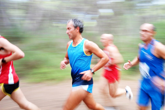 Close-up side view of four men running a marathon through a forest, Apulia, Italy