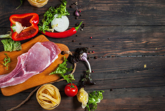 Italian food background, with meat, tomatoes, spaghetti, garlic, peppercorns, chili pepper on wood table