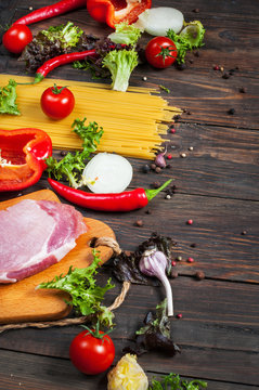 Italian food background, with meat, tomatoes, spaghetti, garlic, peppercorns, chili pepper on wood table