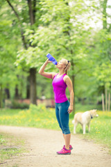 Woman running and jogging with dog in green summer park and wood