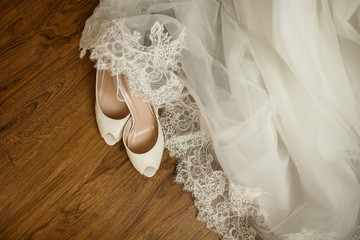 Wedding accessories. Bridal shoes, white dress and veil on the wooden floor at wedding morning...