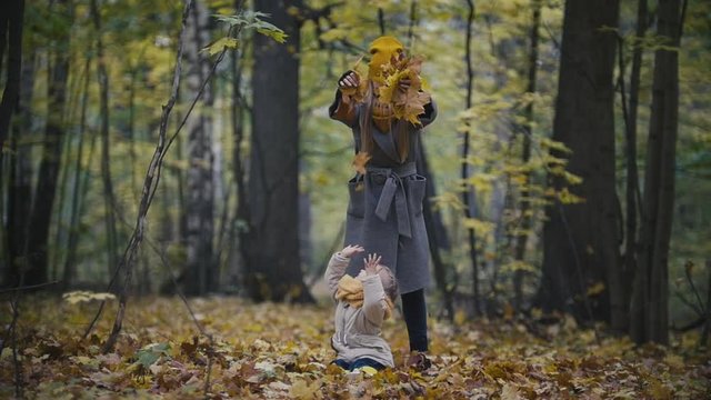 Happy family concept - little daughter with her mother plays with yellow leaves in autumn park, slow-motion
