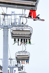 Legs of skiers and snowboarders riding on a cable chair lift in cloudy snowy winter mountains scenic vertical close up