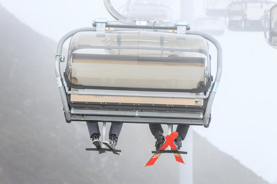 Legs of two ski riders climbing on a cable chair lift in cloudy snowy winter mountains close up