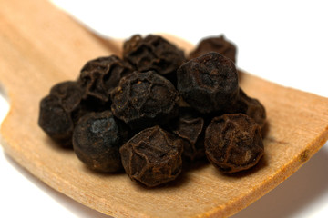 black pepper on wooden spoon. closeup on white