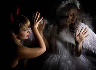 Portrait of angel and devil womans on a dark background, behind transparent glass covered by water...