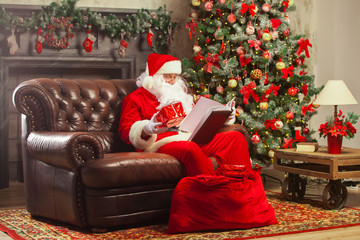 Obraz na płótnie Canvas Santa Claus sitting at his home in a comfortable chair and reading letter. Christmas.