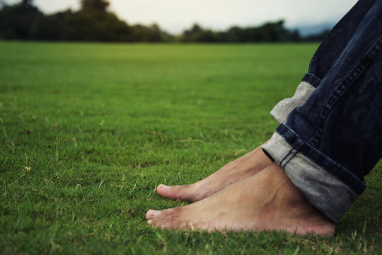 Man feet relaxing on grass enjoying in a day in a park with sky background, Thailand