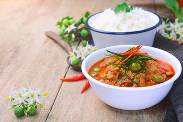 thai red curry fried with pork and coconut milk (panaeng) on white bowl with rice decorated by turkey berry and flower on wooden table.