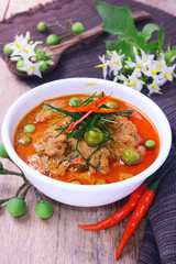 thai red curry fried with pork and coconut milk (panaeng) on white bowl with rice decorated by turkey berry and flower on wooden table.