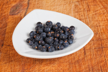 Frisch geerntete Wacholderbeeren in weißer Schale auf altem Holz