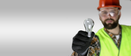 Worker in a helmet and protective clothing with a light bulb in