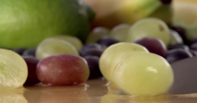 Slicing a grape in half using a sharp kitchen knife. Filmed with selection of fruit in background and on a wooden chopping board. Filmed in slow motion.