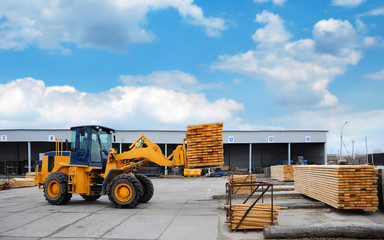Orange forklift transports the boards at the plant for woodworking.