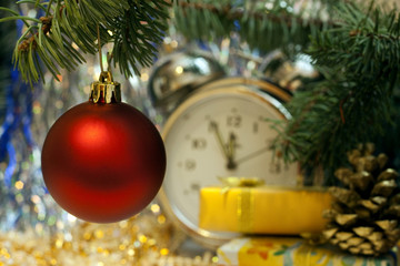 Christmas and New Year`s vintage clock showing five to midnight. Gold gift box with gold bow, retro big toy red glass ball, fir cones and tree branches. Greeting card Background with holiday tinsel.