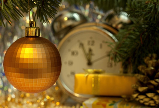 Christmas and New Year`s vintage clock showing five to midnight. Gold gift box with gold bow, retro big toy gold glass ball, fir cones and tree branches. Greeting card Background with holiday tinsel.