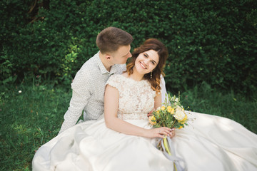 Stylish couple of happy newlyweds walking in the park on their wedding day with bouquet