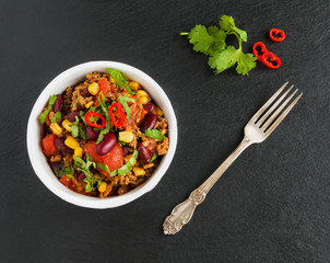 Chili con carne in a white ceramic bowl on black stone background. Cooked with ground beef,...
