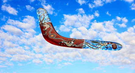 Australian boomerang flies in sky against of pure white clouds. - obrazy, fototapety, plakaty