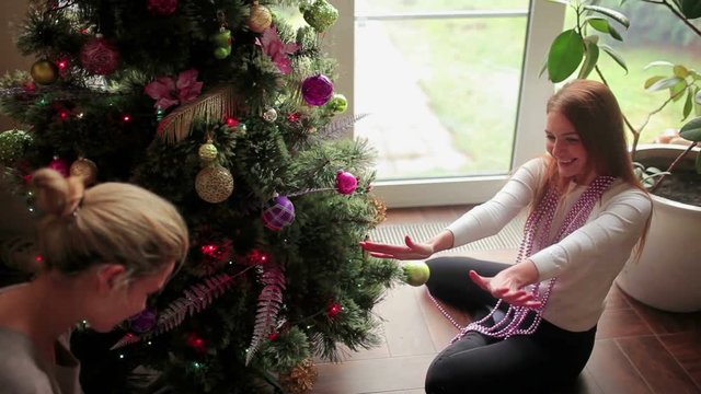 Sisters sit on floor and decorate Christmas tree